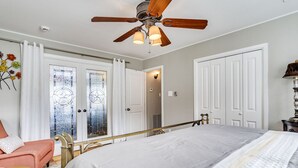 Un dormitorio con cama, ventilador de techo, ventana con cortinas y una puerta.