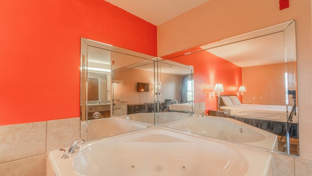 A modern bathroom with a large bathtub, a double mirror, and a red accent wall. - Fairway Inn (La Porte)