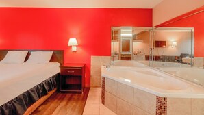 A hotel room with a bed, a nightstand, a large mirror, and a bathtub. - Fairway Inn (La Porte)