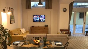 A living room with a sofa, dining table, chairs, a TV, and a window. - SCIESA 24 APARTMENTS - CIR 023091-LOC-02700 - CIN IT023091C28NS3TMSQ (Verona)