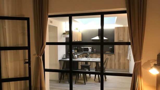 A modern room with a large window, a bed with patterned bedding, and a view of a kitchen area with a dining table and chairs. - SCIESA 24 APARTMENTS - CIR 023091-LOC-02700 - CIN IT023091C28NS3TMSQ (Verona)