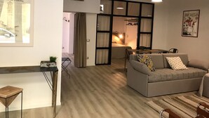 A modern living room with a grey sofa, a small table, and a hanging light fixture. There is a framed picture on the wall and a window with curtains. - SCIESA 24 APARTMENTS - CIR 023091-LOC-02700 - CIN IT023091C28NS3TMSQ (Verona)