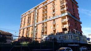 Edifici residencial de diversos pisos amb balcons, entrada a terra visible i cel blau.