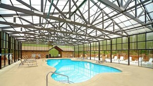 Una piscina interior con techo de vidrio, sillas de descanso y una pequeña estructura de edificio.
