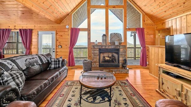 Interior acogedor de una cabaña con chimenea, paredes de madera, un sofá y un televisor.