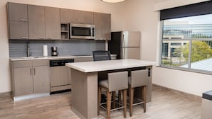 Una cocina moderna con armarios grises, un microondas integrado, un refrigerador y una zona de comedor con taburetes de bar.