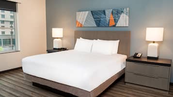 A hotel room with a large bed, two bedside tables with lamps, a nightstand with a phone, and a modern abstract painting on the wall.