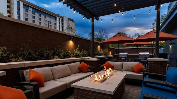 Un patio al aire libre con un hogar a leña de ladrillo, asientos acolchados y luces colgantes.