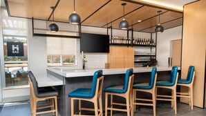 Un área de bar moderna con una barra larga, taburetes y un televisor montado en la pared.