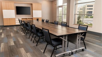 A conference room with a long table, chairs, a flat-screen TV, and large windows.