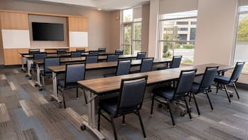 Un salón de conferencias con una gran mesa, sillas, una pantalla de televisión y ventanas que dan a vistas de edificios y árboles.