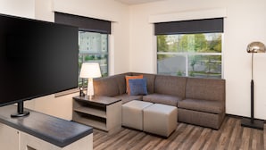 Una habitación de hotel moderna con un sofá modular, un televisor de pantalla plana, una lámpara y vistas al exterior.