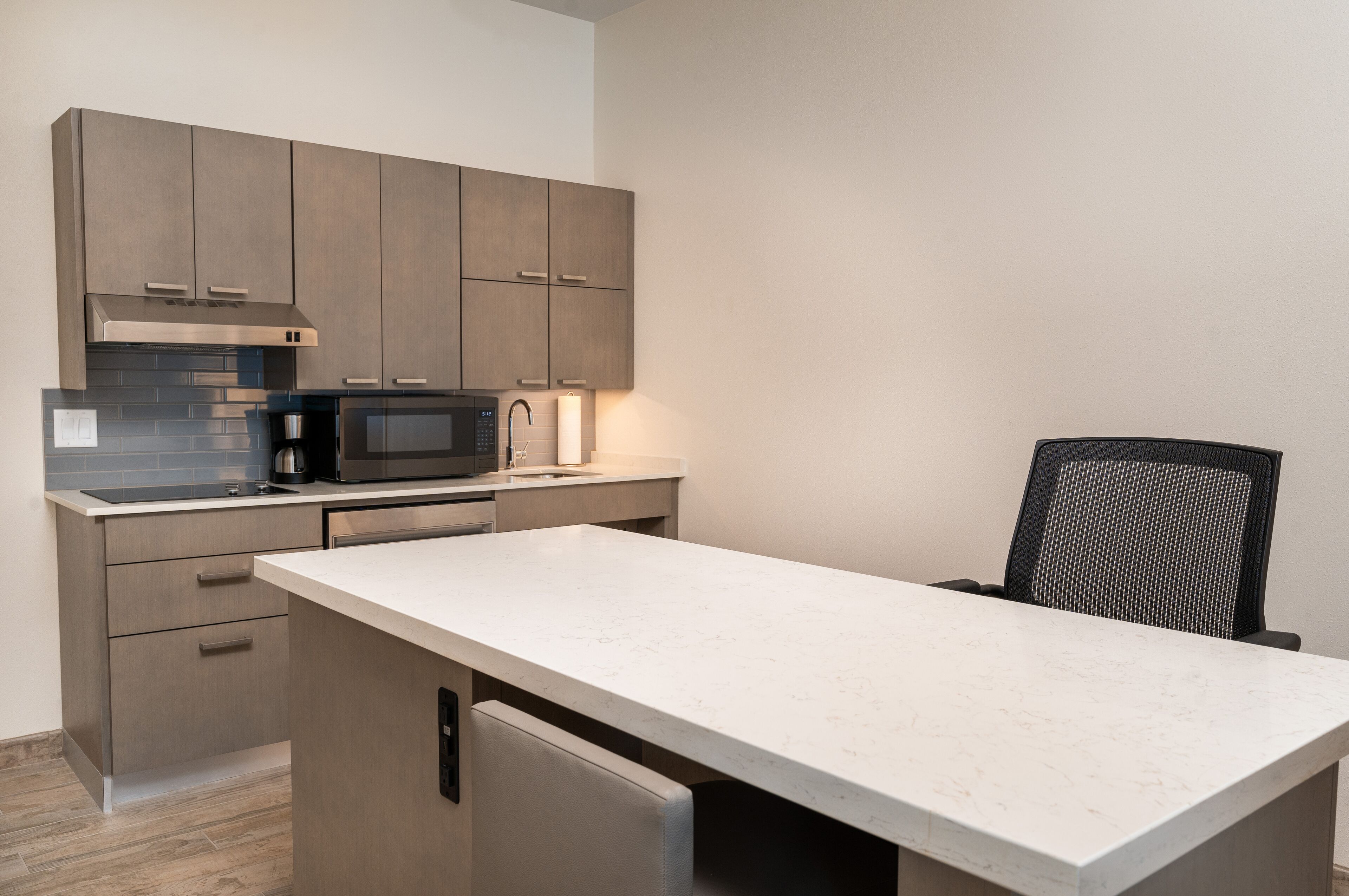 A modern kitchen with grey cabinets, a stainless steel range hood, a microwave, and a built-in dishwasher.