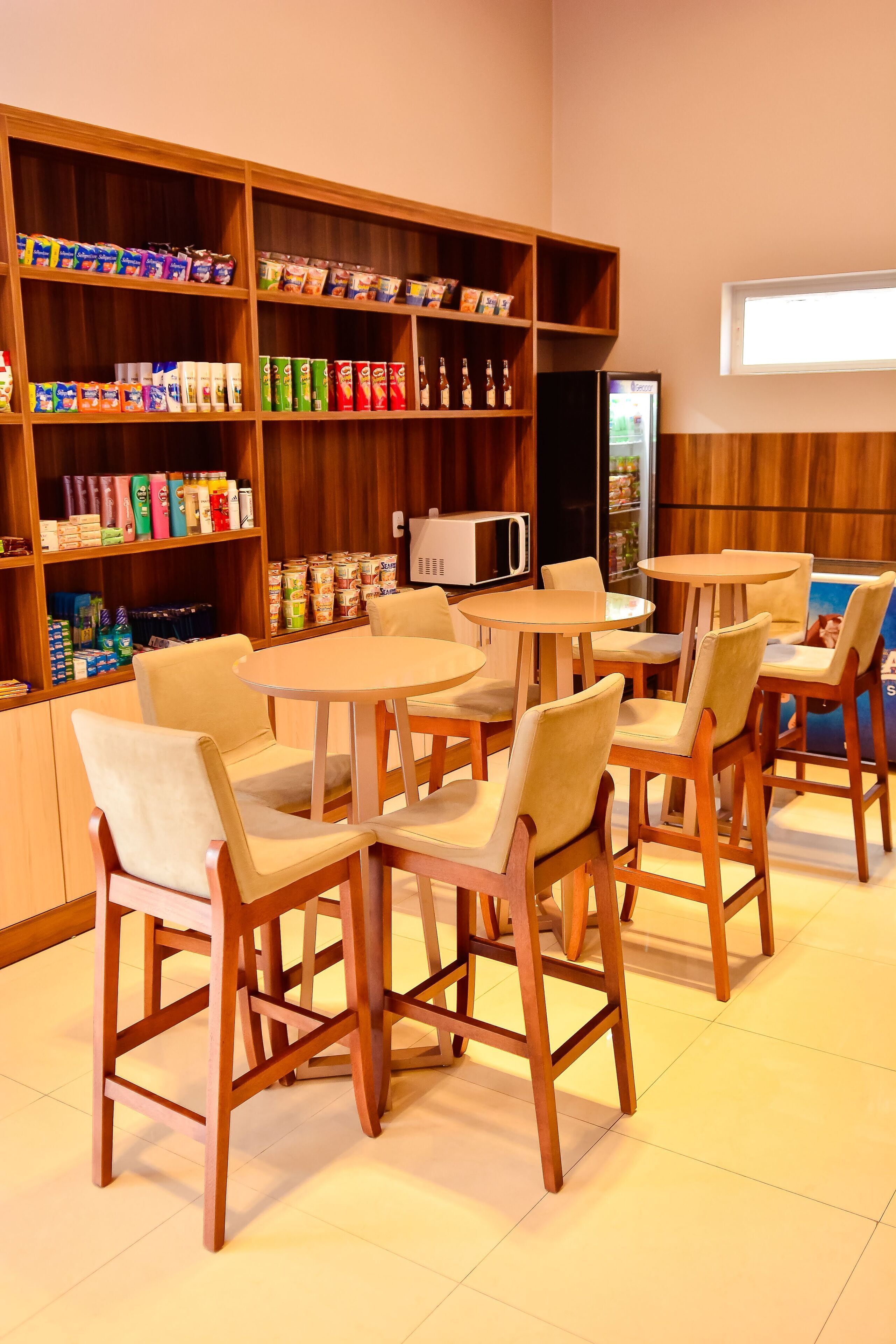 A cafe with wooden chairs and tables, shelves with snacks and beverages, and a microwave.