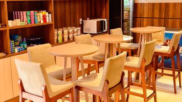 A cafe with wooden chairs and tables, shelves with snacks and beverages, and a microwave.