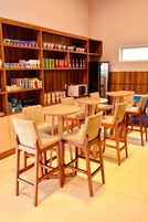 Um café com cadeiras e mesas de madeira, prateleiras com lanches e bebidas, e um micro-ondas.