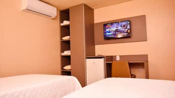 A hotel room with two beds, a TV mounted on the wall, a minibar, and a built-in air conditioner.