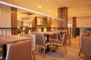 Interior moderno de restaurante com mesas e cadeiras de madeira, divisória de vidro e luminária pendente decorativa.