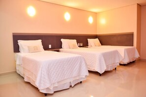 A hotel room with two beds, each with a white bedspread and pillows, and wall-mounted light fixtures.