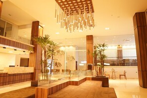 Um lobby de hotel moderno com balcão de recepção, área de estar e plantas decorativas.