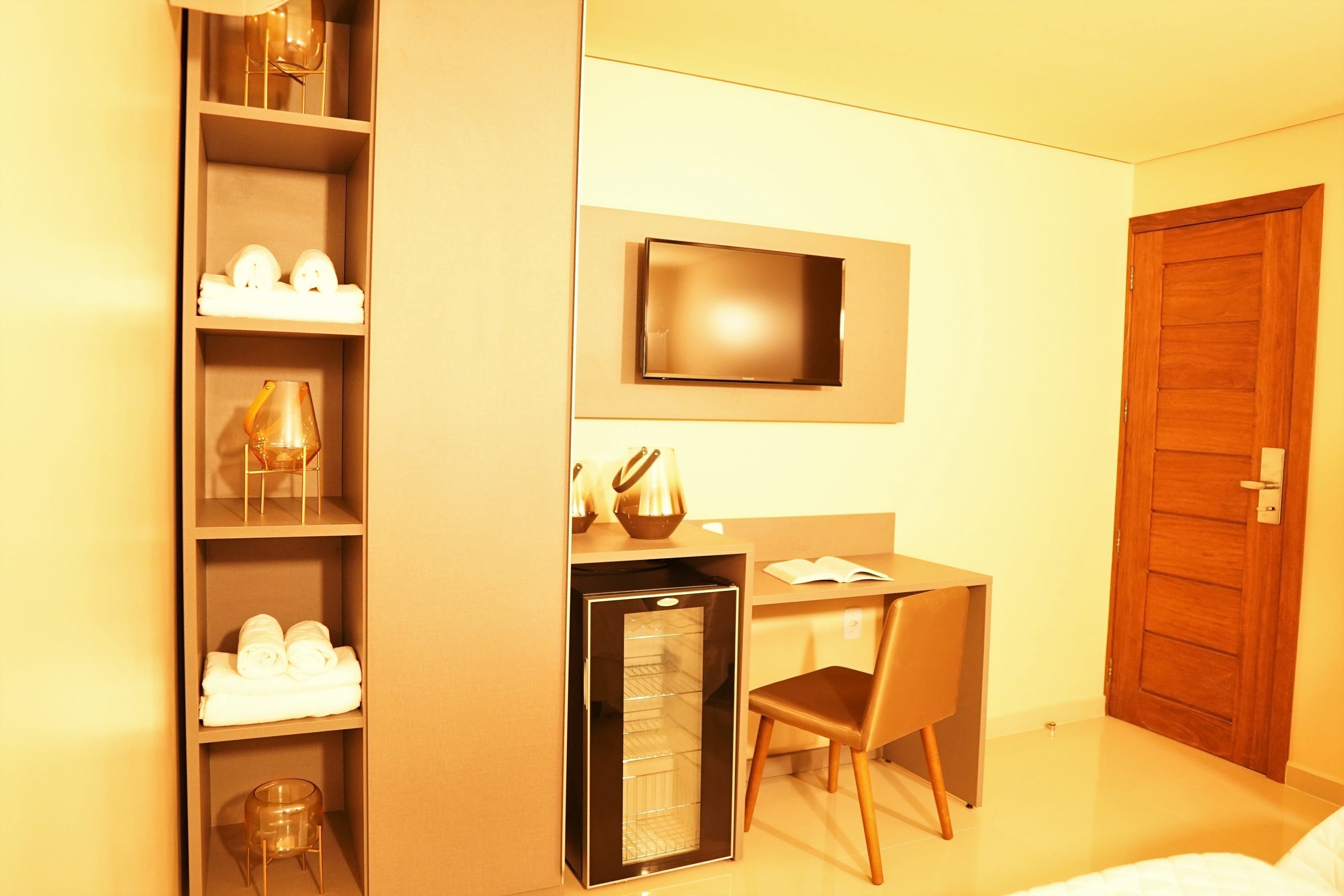 A compact hotel room with a bed, a desk, a television, a minibar, and a wardrobe.