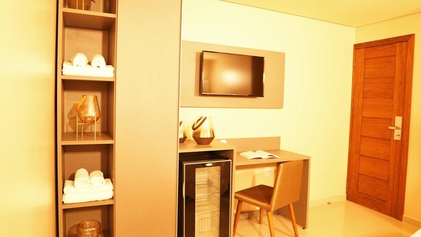 Een kleine hotelkamer met een bed, een bureau, een televisie, een minibar en een kledingkast.