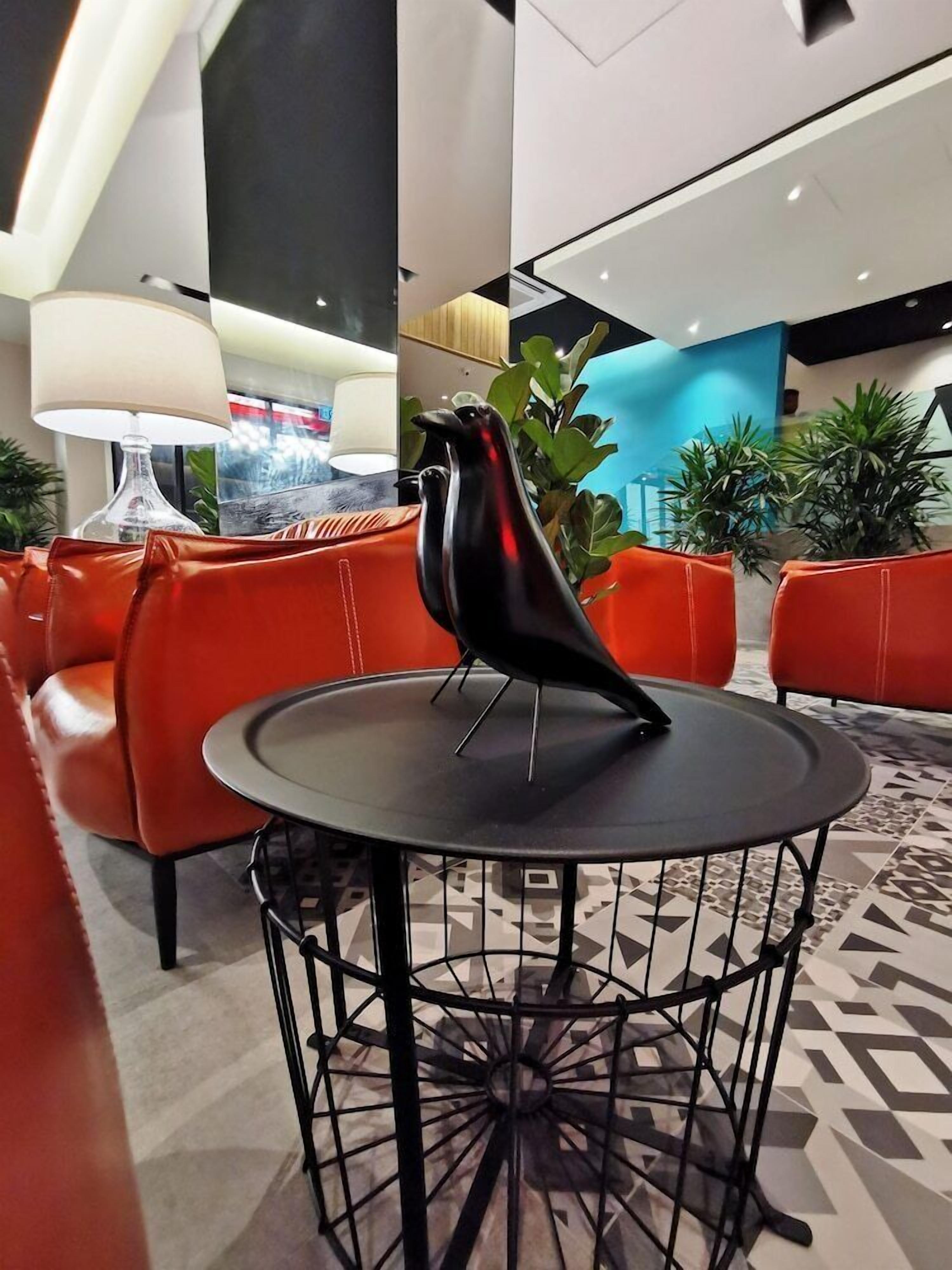 Un vestíbulo moderno con una mesa redonda, asientos de cuero rojo y una escultura decorativa de un pájaro negro.