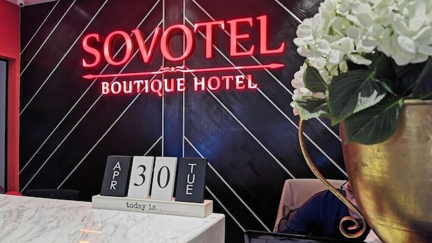 A reception desk at Sovotel Boutique Hotel with a neon sign, a date display, and a vase with white flowers. - Sovotel Conezion Putrajaya (Serdang)