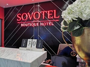 A reception desk at Sovotel Boutique Hotel with a neon sign, a date display, and a vase with white flowers. - Sovotel Conezion Putrajaya (Serdang)
