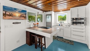 Una cocina con armarios blancos, un refrigerador de acero inoxidable, horno empotrado y techo de madera.