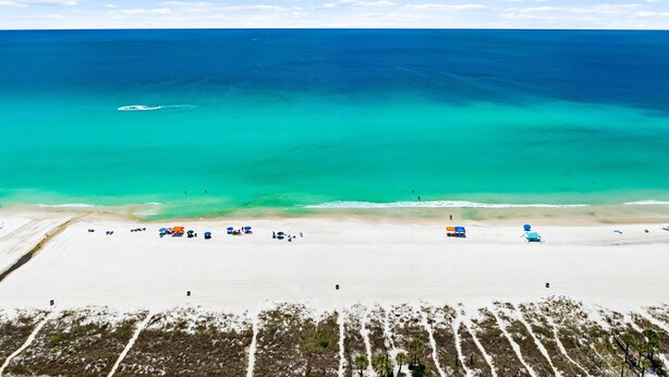 Vista aérea de una playa con aguas turquesas cristalinas, una orilla arenosa y algunas sombrillas.