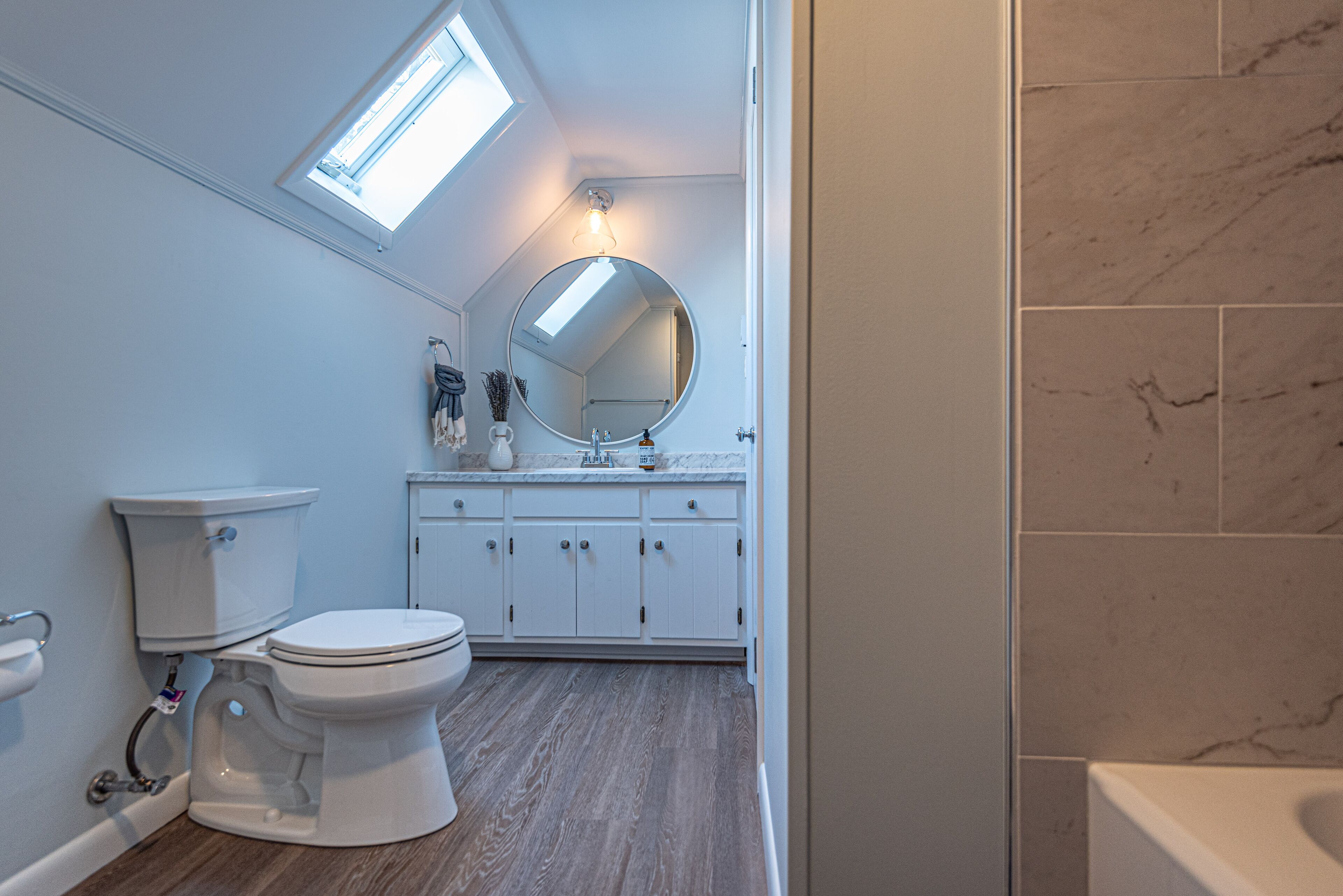 Une salle de bain dotée d’une lucarne, de toilettes blanches et de murs recouverts de carreaux de marbre.