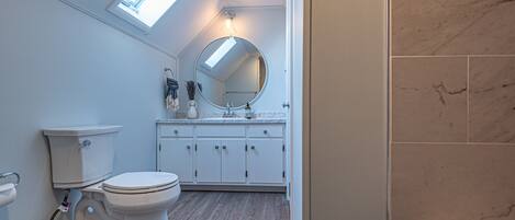 Une salle de bain dotée d’une lucarne, de toilettes blanches et de murs recouverts de carreaux de marbre.