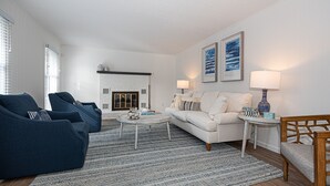 Ein Wohnzimmer mit einem weißen Sofa, blauen Sesseln, einem Couchtisch und einem Kamin.