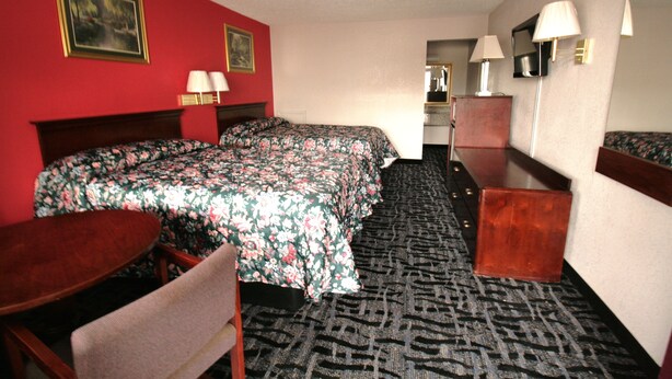 Ein Hotelzimmer mit einem großen Bett, einem Schreibtisch, einem Sessel, einem Spiegel und Teppichboden.