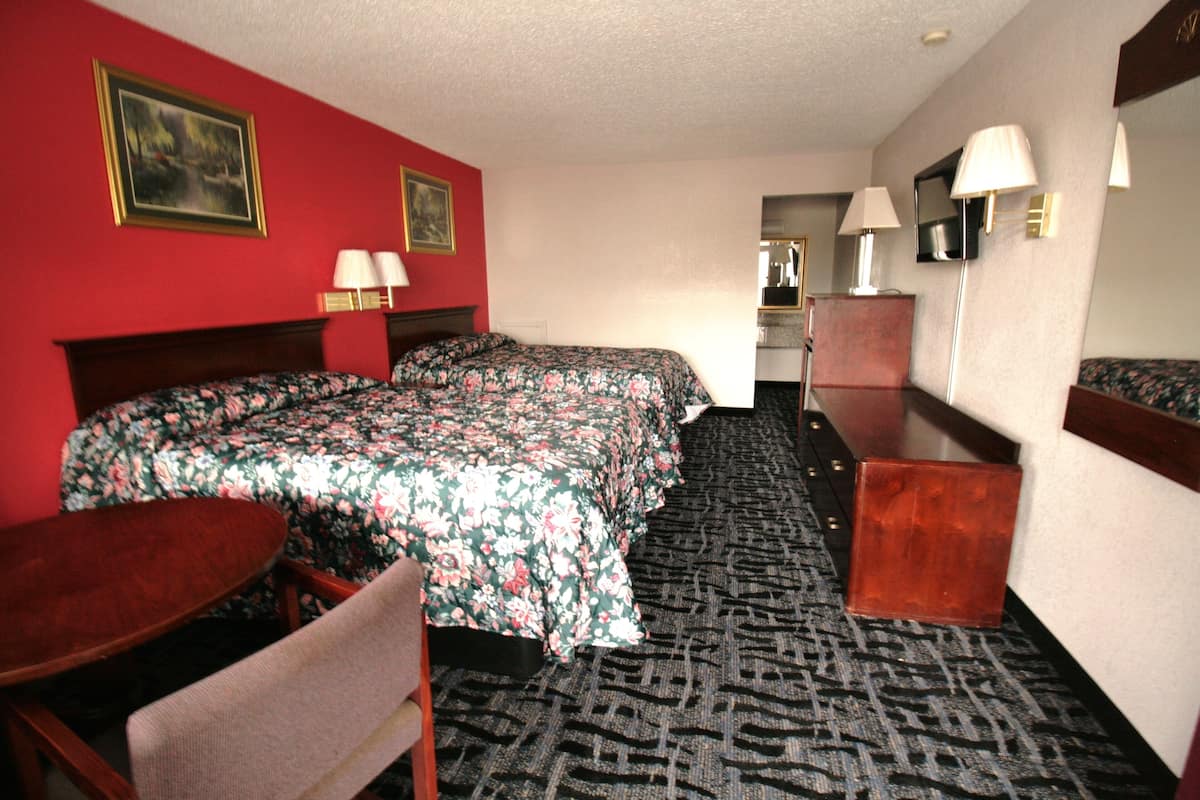 A hotel room with a large bed, a desk, a chair, a mirror, and a carpeted floor.