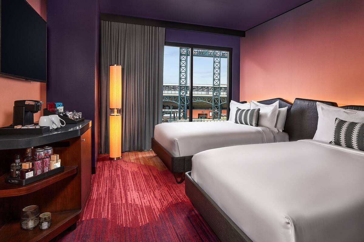 A hotel room with two beds, a desk with a coffee maker, a lamp, and a view of a bridge.