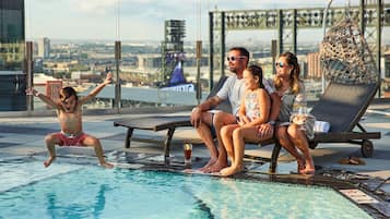 Una piscina en la azotea con vista a la ciudad, sillas de descanso y barandilla de cristal.