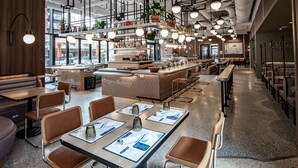 A modern restaurant interior with high ceilings, exposed ductwork, and a central bar area. - The Rally Hotel at McGregor Square (Denver)