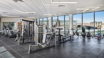 A gym with various exercise machines, large windows, and a view of a bridge and cityscape.