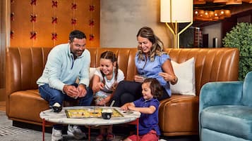 A family playing board games on a brown leather couch with a marble coffee table in a modern lobby with wooden paneling and a chandelier.