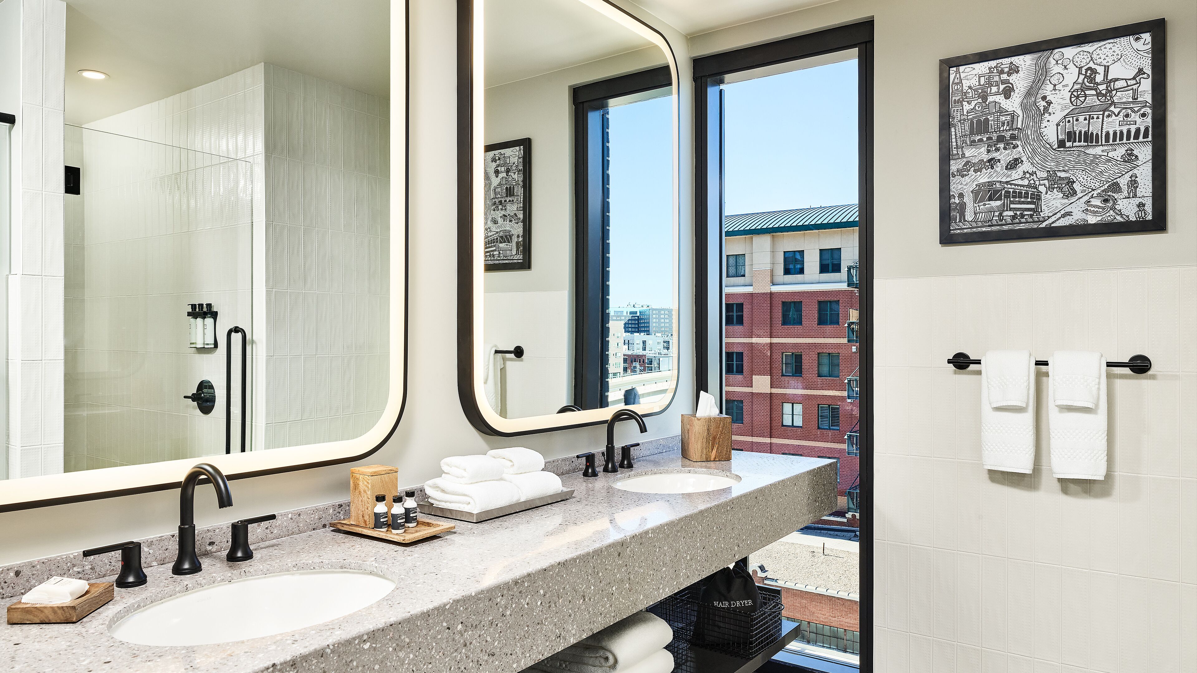 A modern bathroom with a large mirror, two sinks, and a view of a cityscape through the window.