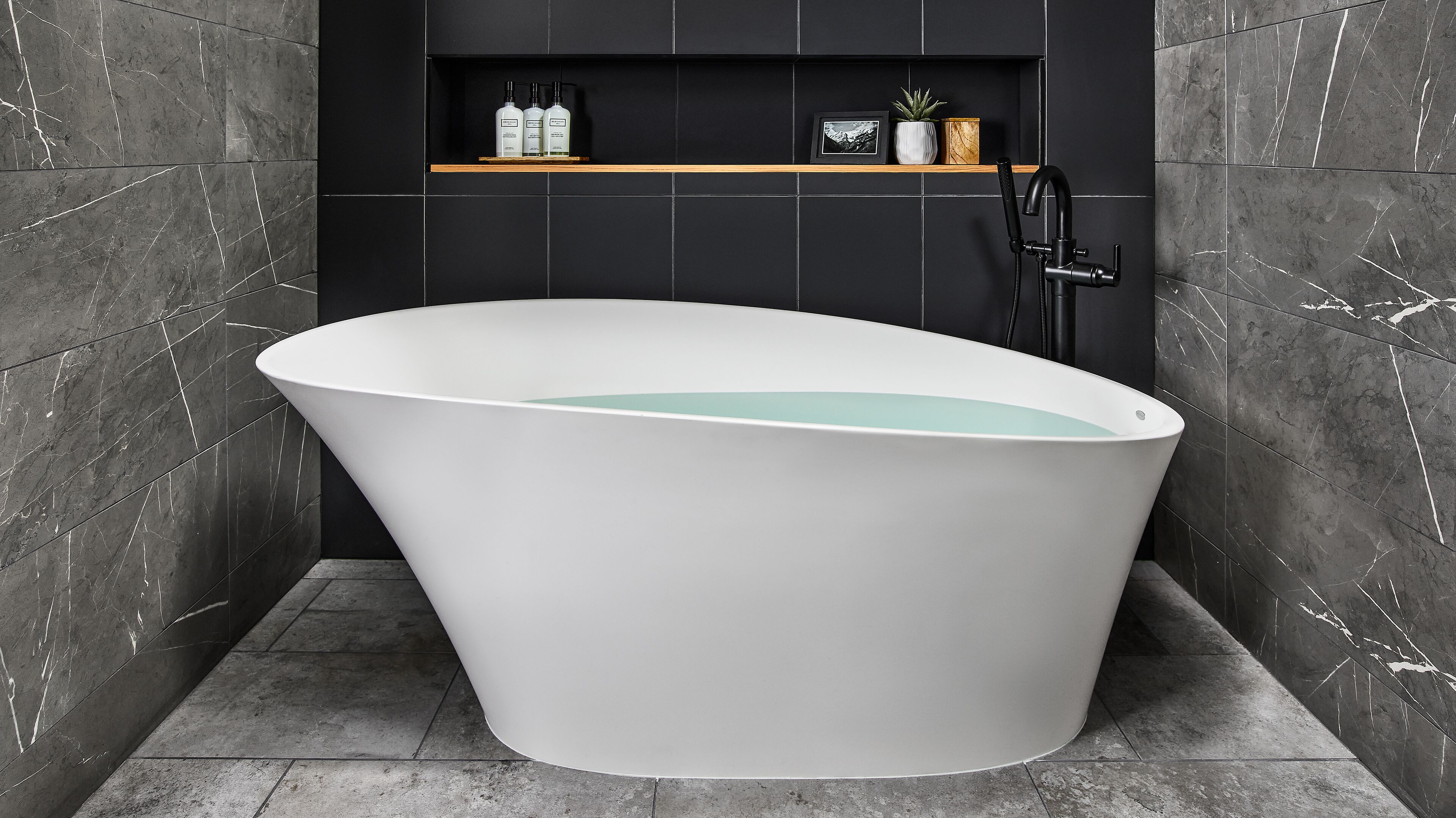A modern bathroom with a freestanding bathtub, a black wall-mounted faucet, and a shelf with toiletries.