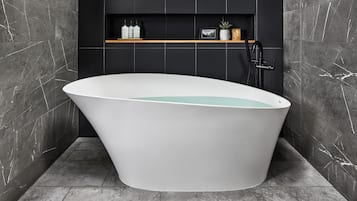 A modern bathroom with a freestanding bathtub, a black wall-mounted faucet, and a shelf with toiletries.