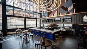A modern bar area with a central island, multiple seating options, and large windows offering views of the cityscape. - The Rally Hotel at McGregor Square (Denver)
