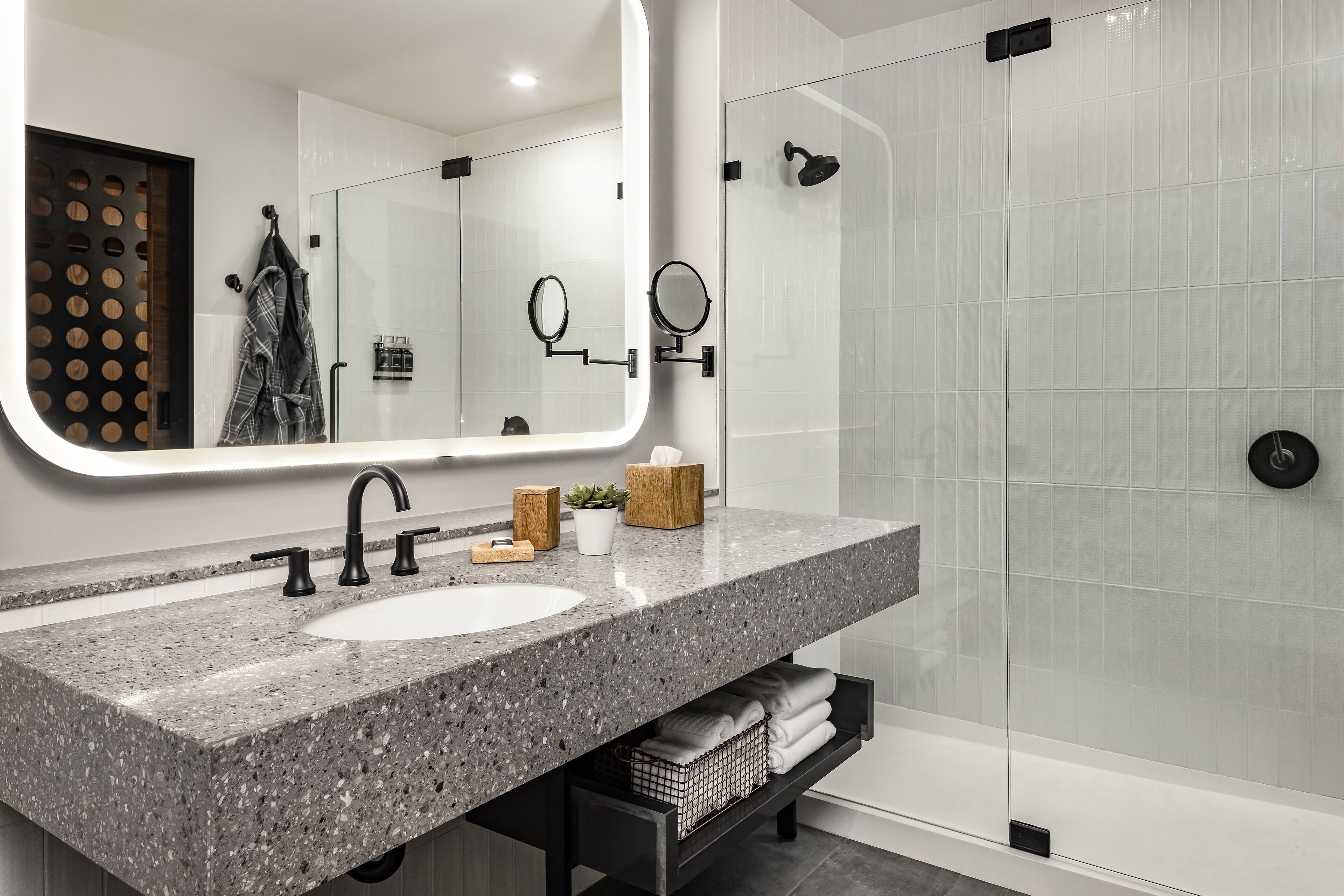 A modern bathroom with a granite countertop sink, a large mirror, a handheld showerhead, and a glass-enclosed shower.
