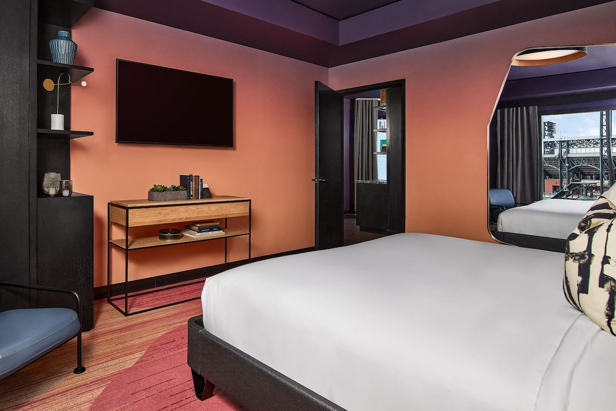A hotel room with a bed, a desk with a computer, a chair, and a TV on the wall.