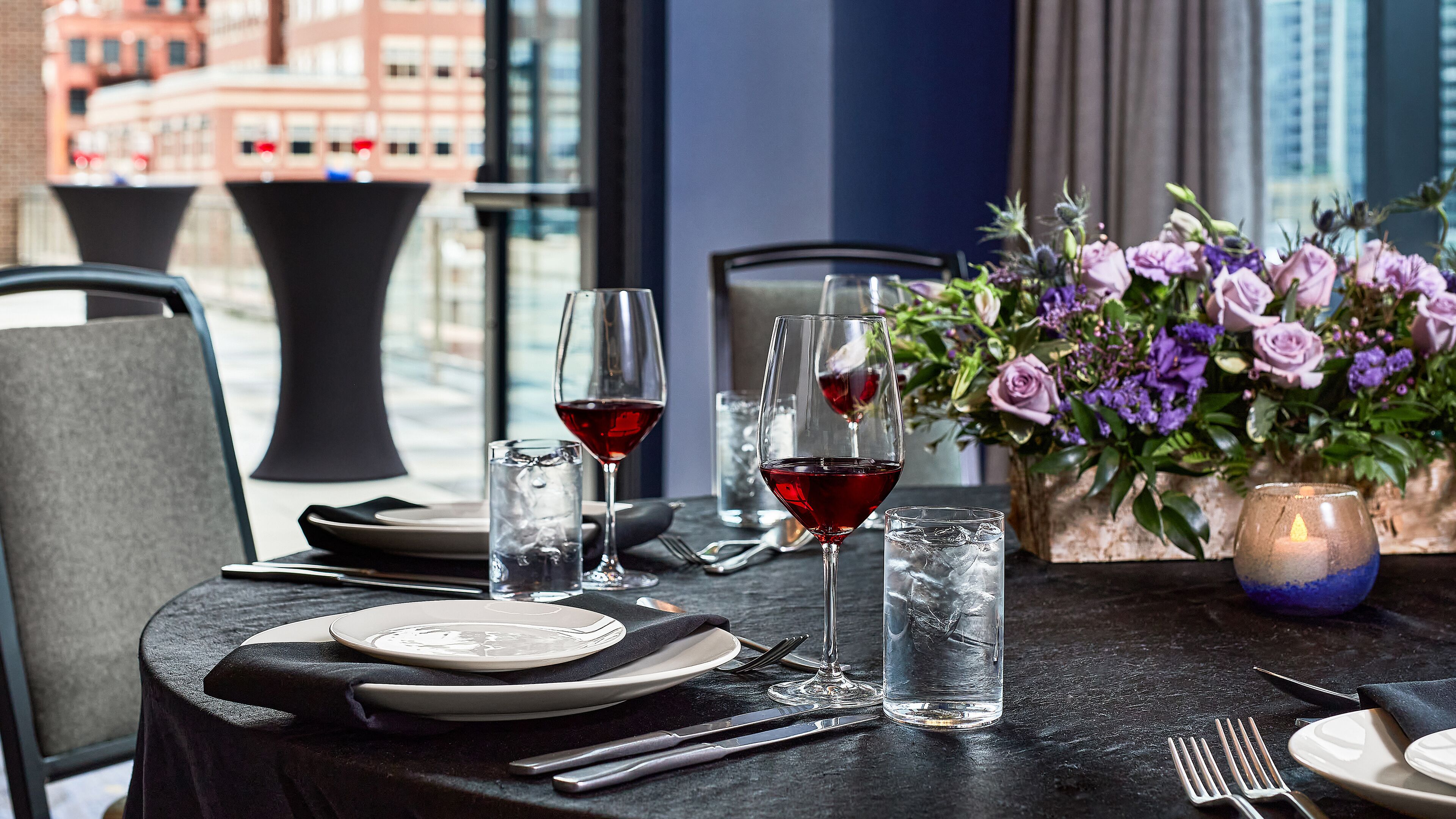 A table set for dining with plates, cutlery, and glasses of red wine.