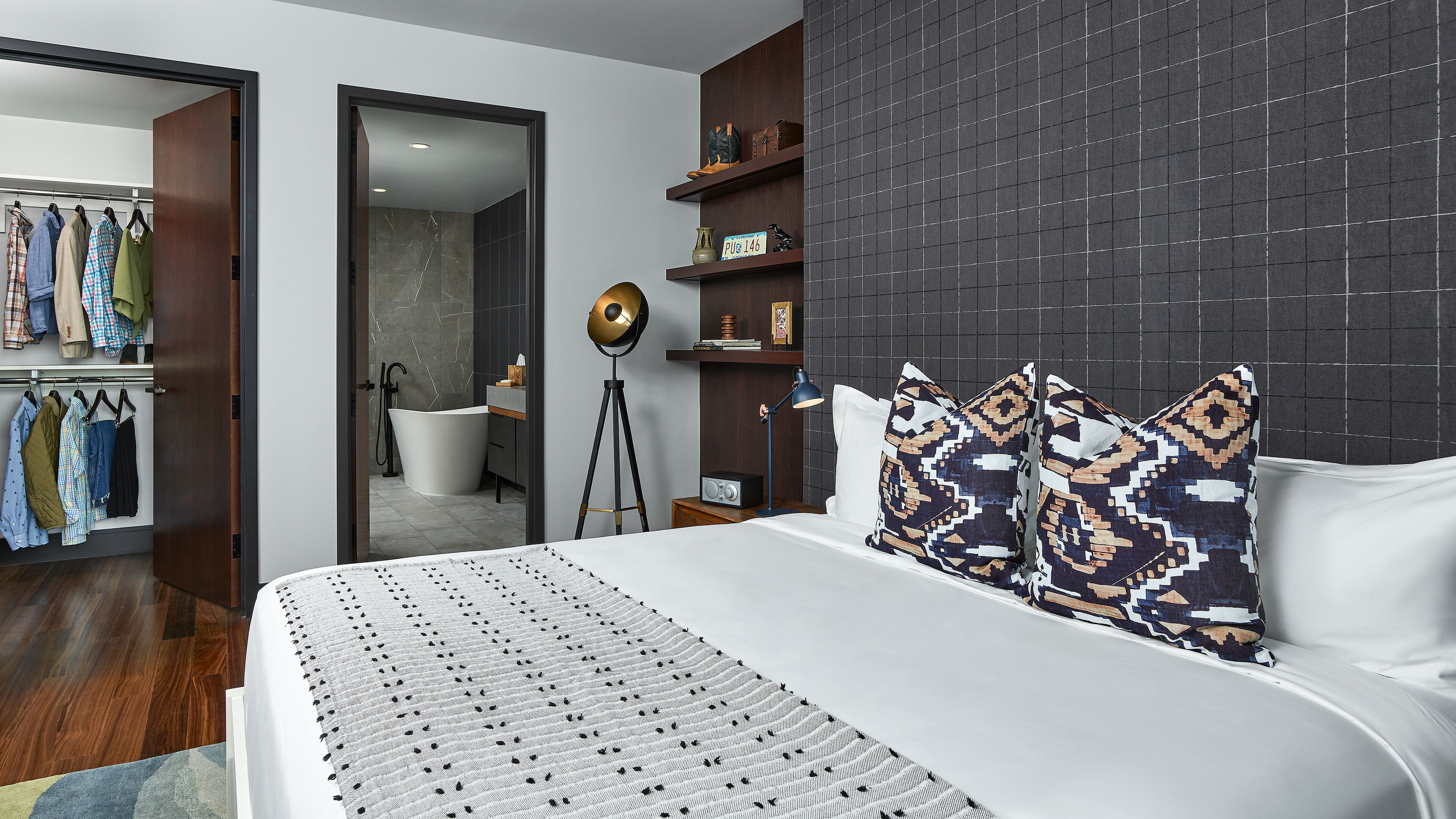 A modern bedroom with a large bed, a wardrobe, a vanity, and a bathroom visible through an open door.