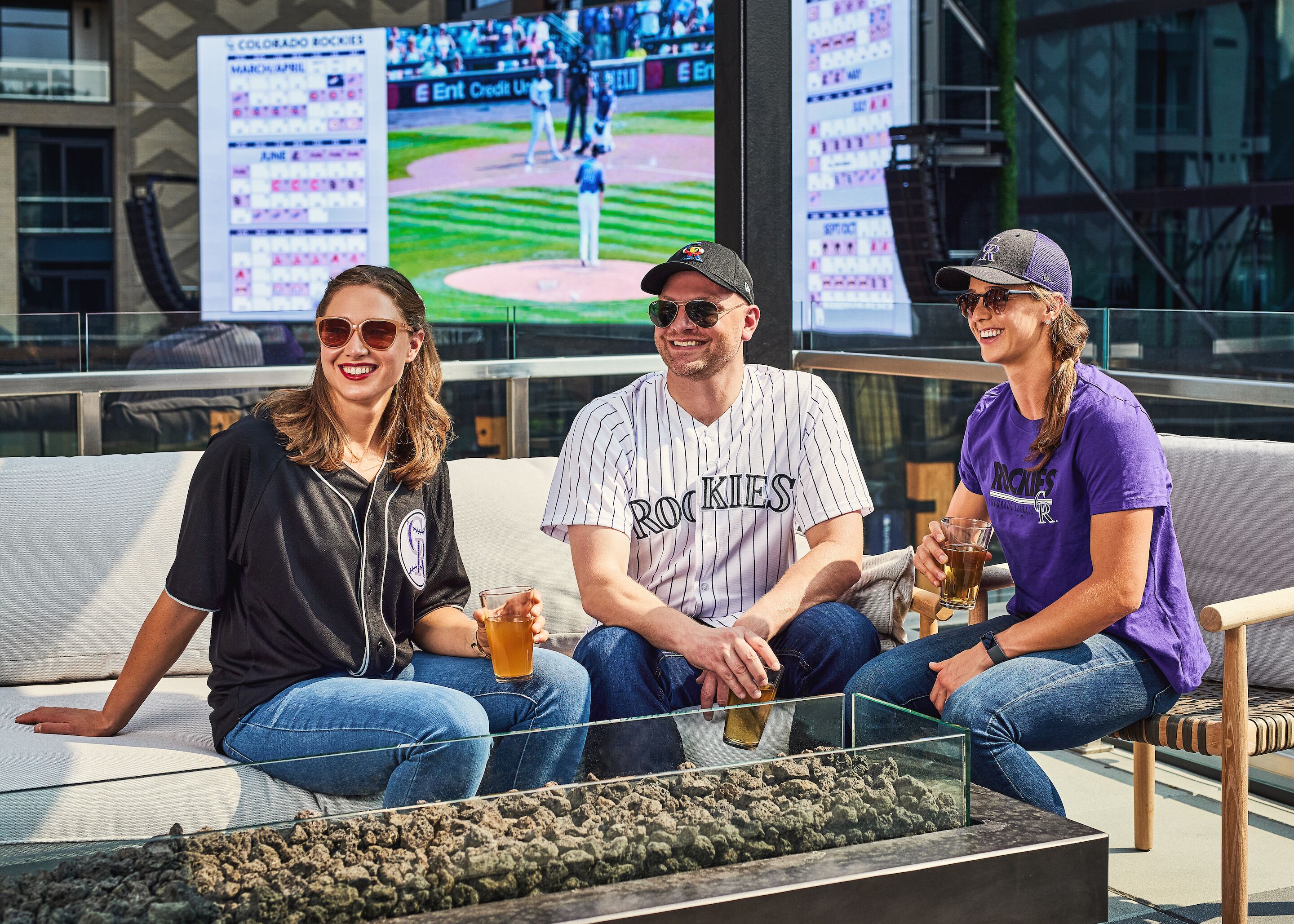 Kolme ihmistä istuu sohvalla, ja heidän takanaan televisiossa näkyy baseball-ottelu.